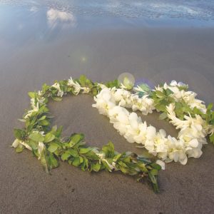 浜辺にハートの形で置かれた、マイレのレイと、白い花のレイの写真