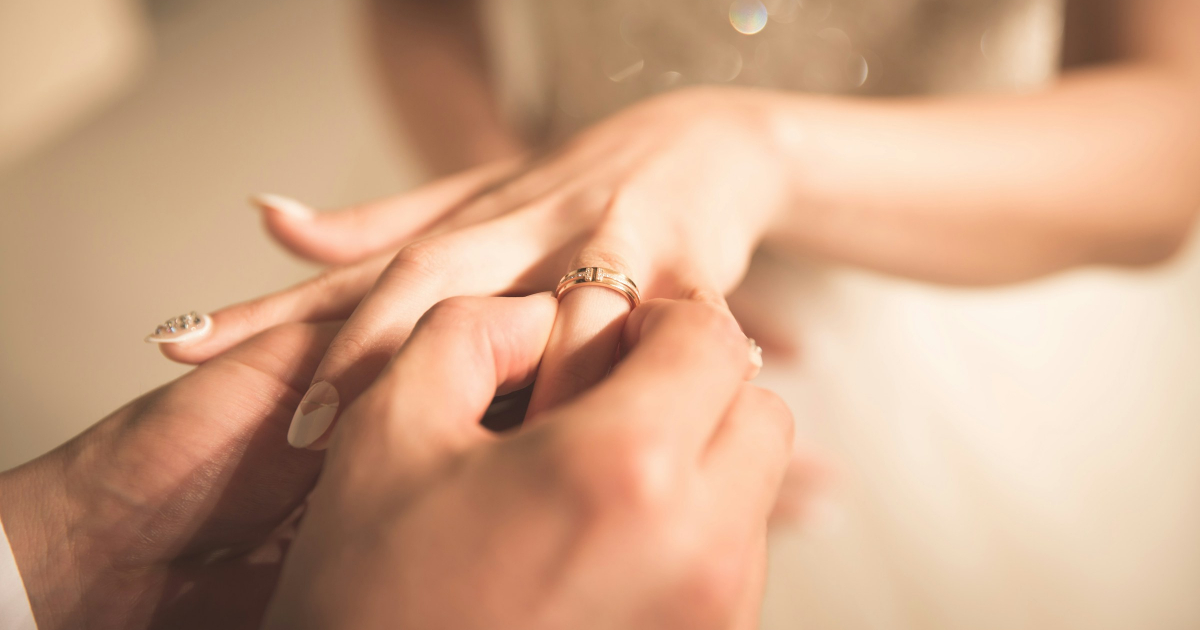 男性が女性の左手薬指に結婚指輪をはめる写真