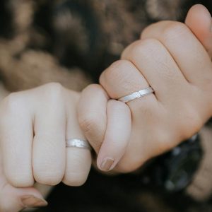 薬指にペアリングをはめたカップルが小指を結んでいる写真