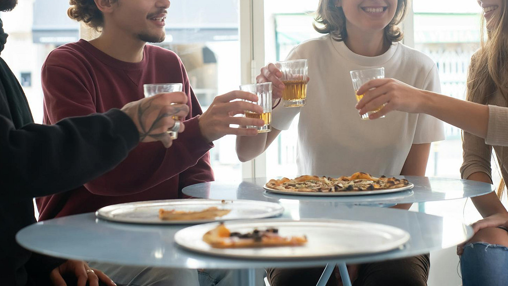 男女4人の友人がテーブルを囲み、グラスを片手に笑顔で乾杯している。