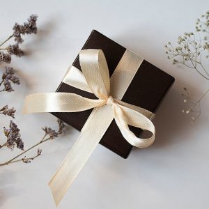 ジュエリープレゼントの選び方を象徴する、リボンが結ばれた黒いギフトボックスとドライフラワーが置かれたアイキャッチ画像。