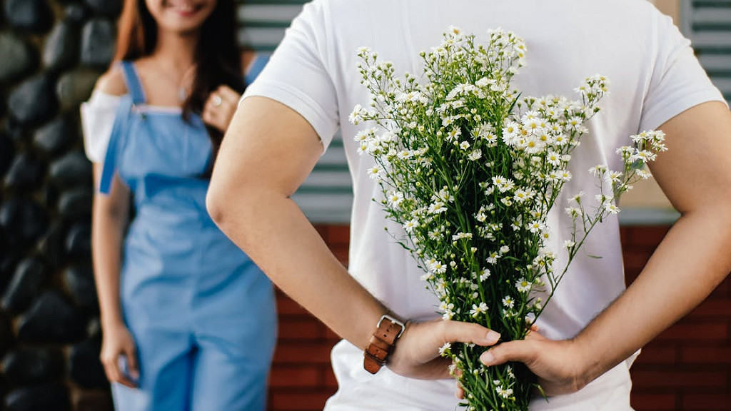 サプライズプレゼントする場面。笑顔の女性を前に、男性が背中に花束を隠している。