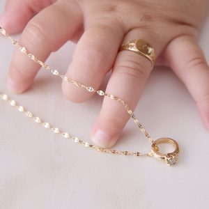 赤ちゃんの手に着けたイニシャルシグネットベビーリングと、隣に置かれたチェーン付きバースデーストーンベビーリング